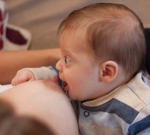 Baby with chin and lower lip touching breast, opening mouth wide to stretch over nipple