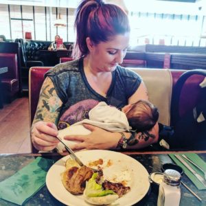 Mother eating in a restaurant while breastfeeding her small baby