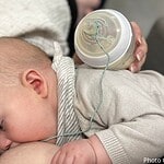 baby at breast, being fed milk via tube coming from a bottle